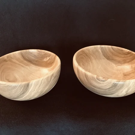 Two light wooden bowls with a distinctive grain set on a dark background.