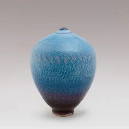 A vessel that is narrow at the top and bottom. The blue colour is pattered with artist markings and becomes more of a gradient into a dark purple at the bottom.