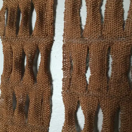 Copper wire weaved into a quilt-like pattern, the woven strips are in sections that contain about four vertical strips and they have negative space between each section.