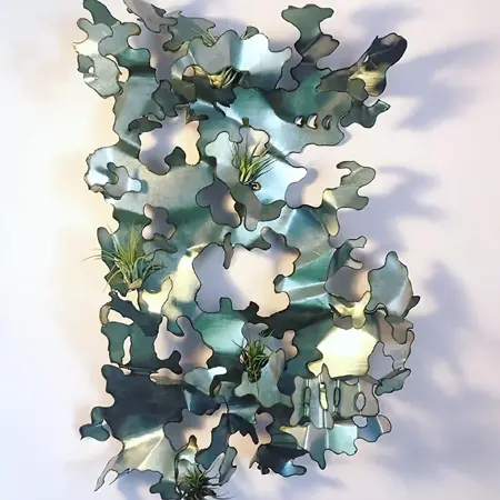 Green and silver metal sculpture with irregular edges, folds, and cuts. Air plants are incorporated into some folds.