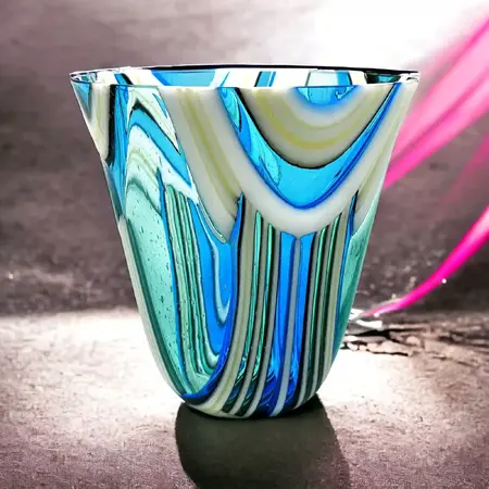 A blue and white glass blown vessel with a geometric line patterning. The vessel is sitting on a black surface.