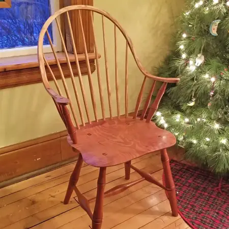 A wooden chair with an arched back, spindles, and arm rests. The warm stain brings out the grain of the wood.