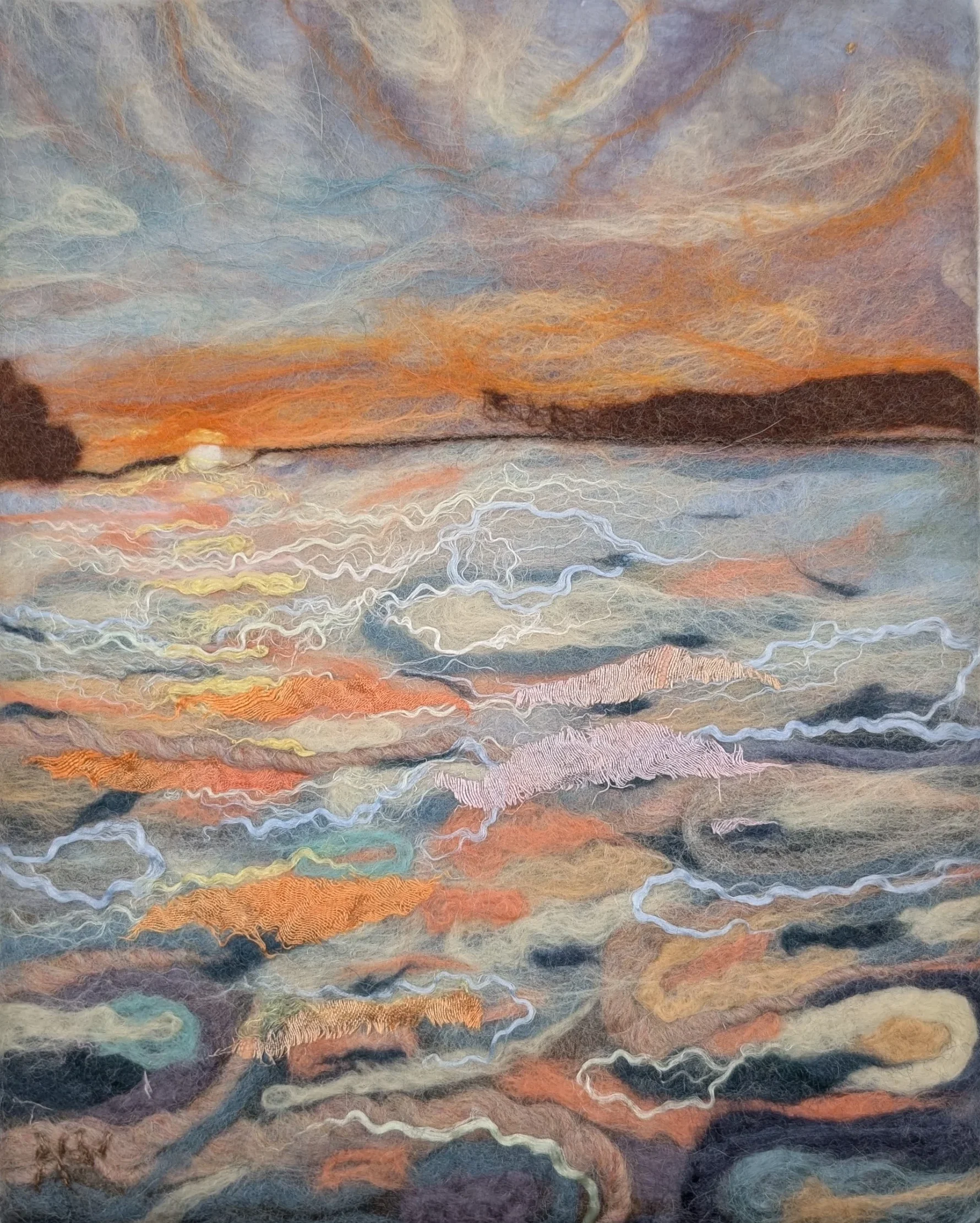 Ann Way-Nee’s felted wool artwork shows a sunset over a body of water with swirling clouds and reflections.