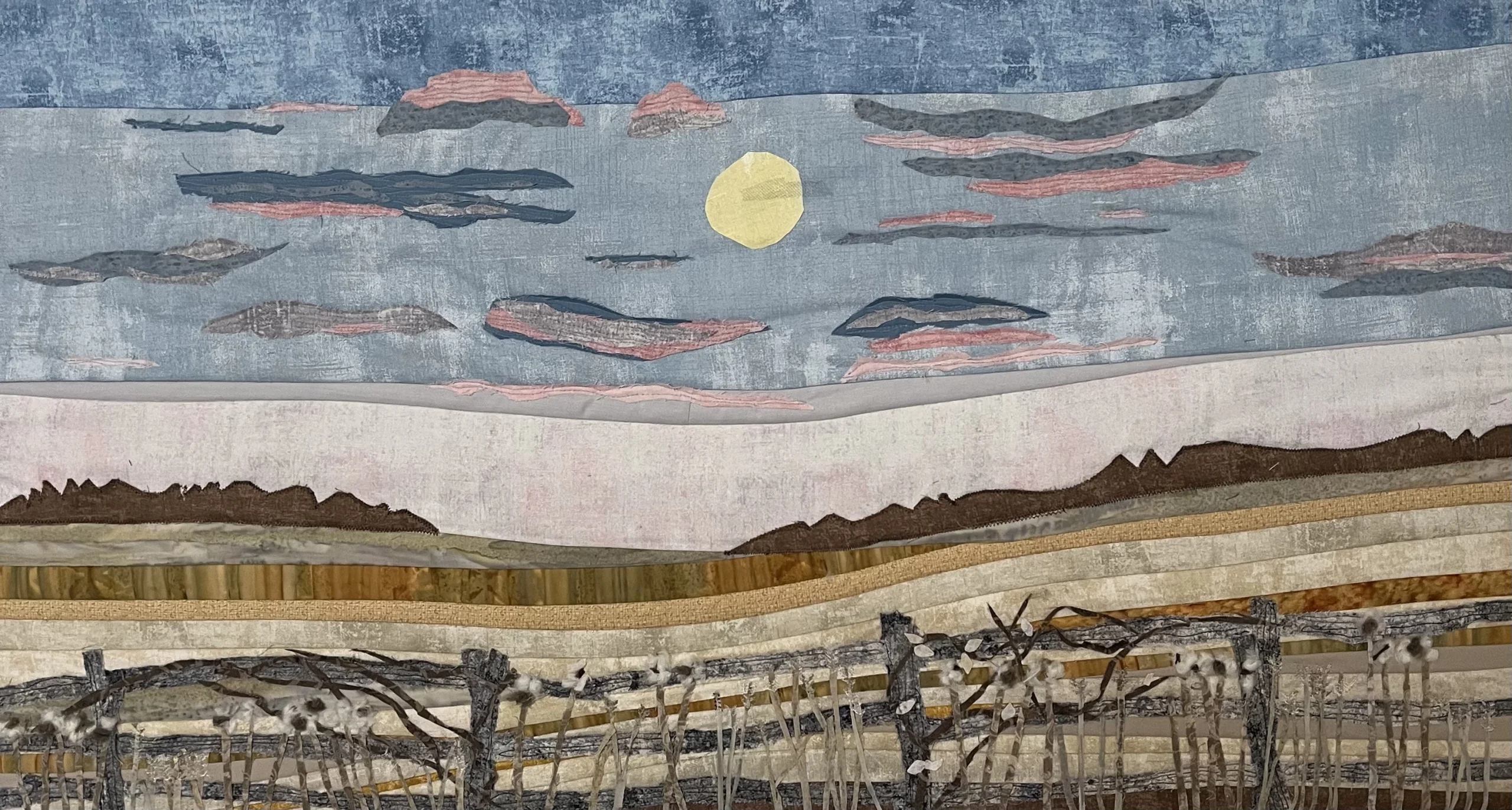 A textile art piece by Cathy Stalkie called Bridgenorth Trail depicting a rural landscape at sunset with a yellow sun, layered hills, and a fence in the foreground.
