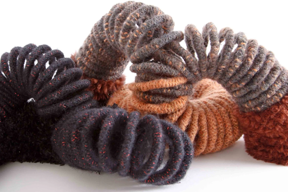 Photograph of knitted wool cord and shear beaver fur inside a slinky in various shades of brown and black arranged on a white surface. Titled “Forgotten Toys” created by Faye Jacobs.