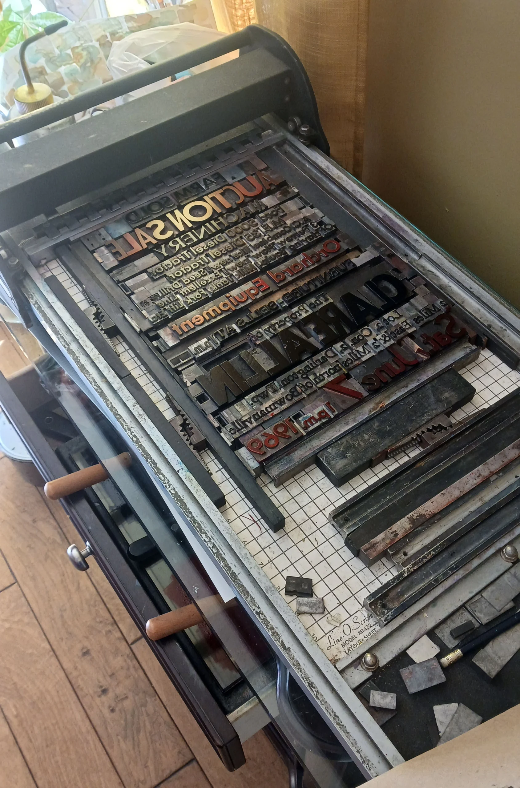 Photograph of a letterpress printing press with metal type arranged on the bed, featuring various fonts and sizes in Jeffrey Macklin’s studio.